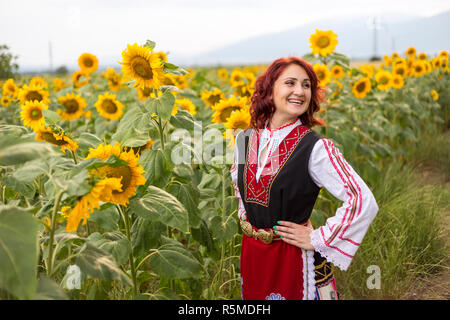 Ragazza in un tradizionale abito bulgaro sentirsi felice in un campo di girasoli Foto Stock