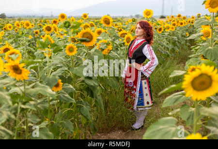 Ragazza in un tradizionale abito bulgaro sentirsi felice in un campo di girasoli Foto Stock