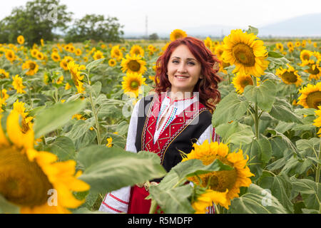 Ragazza in un tradizionale abito bulgaro sentirsi felice in un campo di girasoli Foto Stock