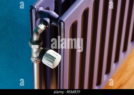 Il termostato su un radiatore di viola e una parete blu Foto Stock