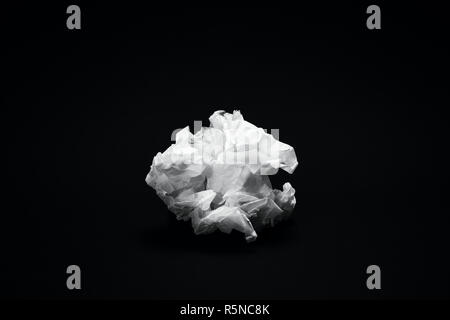 Crumpled white paper texture scuro su sfondo nero sotto il drammatico illuminazione moody Foto Stock