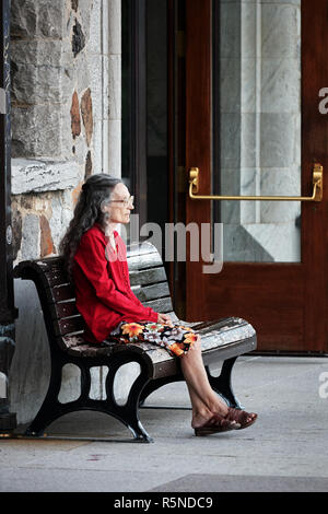 Il sambuco lonely lady al suo anni sessanta si siede sulla panchina di una stazione e attende qualcuno. Uso editoriale. Foto Stock