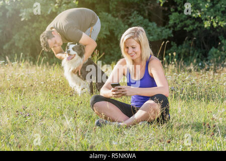 Giovane donna è utilizzando smart phone mentre il suo partner sta giocando con i cani Foto Stock