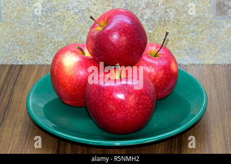 Pila di white-spotted mele rosse su una piastra verde su un di legno marrone, desktop con sfondo astratto, top-laterale vista da vicino Foto Stock