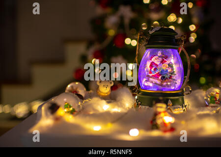 Decorazione di natale, snow dome, globo con decorazioni per la tavola, Santaclaus sulla slitta con il bambino in scena invernale, albero di natale con luci Foto Stock