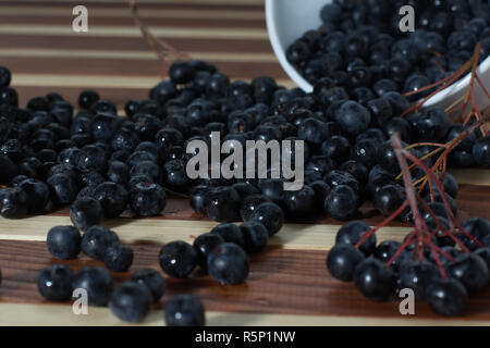 Ciotola piena di aronia versato sul tavolo di legno Foto Stock