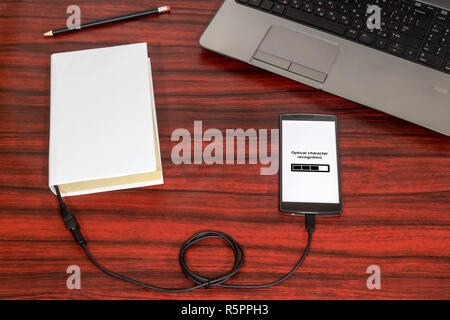 Prenota collegato a uno smartphone attraverso un cavo USB su una scrivania. Riconoscimento ottico dei caratteri barra di caricamento. Foto Stock