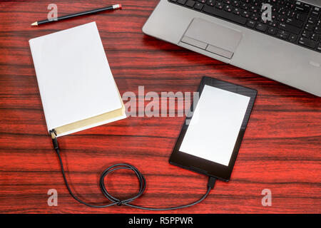 Prenota collegato ad una compressa tramite cavo USB, posa accanto a un computer portatile e matita su una scrivania. Foto Stock