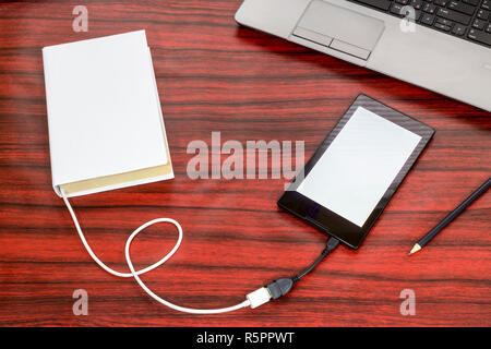 Prenota collegato ad una compressa tramite cavo USB, posa accanto a un computer portatile e matita su una scrivania. Foto Stock