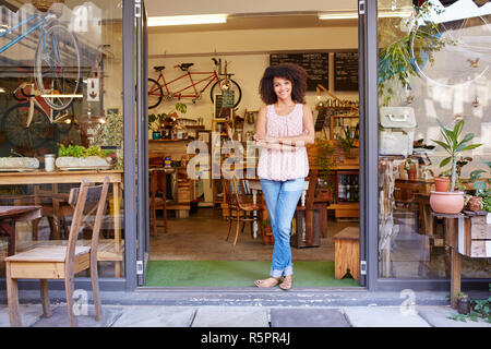 Donna in piedi felicemente in ingresso del suo coffee shop Foto Stock