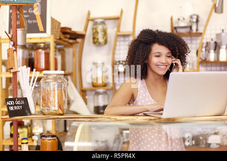 Sorridente coffee shop proprietario digitando su un laptop mentre si parla Foto Stock