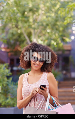 Donna in occhiali da sole l'invio di un messaggio sul suo telefono Foto Stock