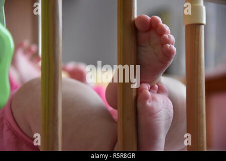 Baby, infantili piedi spuntavano attraverso le rotaie di una culla, lettino, splendido sfondo per scheda, banner, wallpaper design Foto Stock