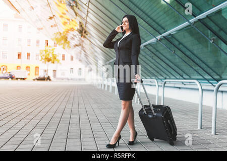 Giovane donna di affari con il telefono cellulare e la valigia in una cornice urbana Foto Stock