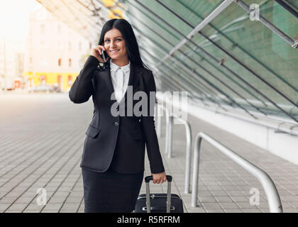 Giovane donna di affari con il telefono cellulare e la valigia in una cornice urbana Foto Stock