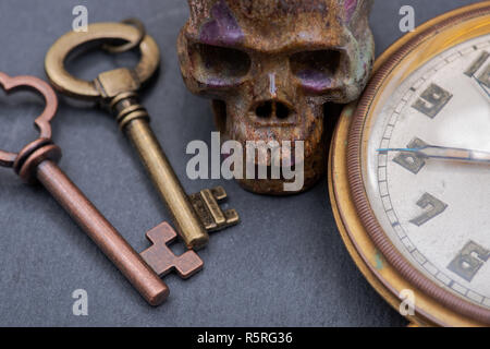 Panta Rhei concetto: antico orologio da tasca, old vintage tasti in metallo e pietra scolpita sul cranio di pietra naturale dello sfondo. Foto Stock