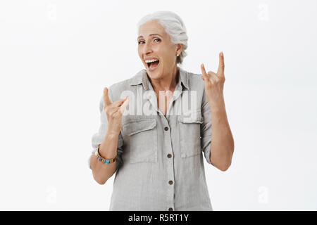 Vita-up shot del carismatico eccitato e felice old Lady sensazione di adolescente con anima giovanile di ridere con gioia che mostra il rock'n'roll segno am permanente Foto Stock