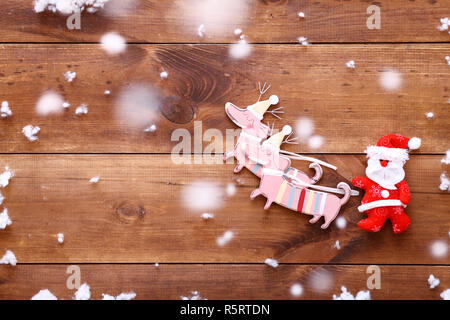 Rosso giocattolo divertenti Babbo Natale a cavallo con slitta di cervi sul marrone sullo sfondo di legno ricoperta di neve, sposarsi Merry Xmas holiday card, buyi Foto Stock