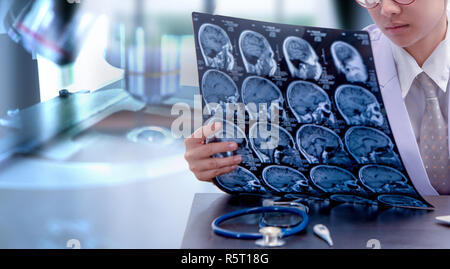Giovani donne medico tenendo MRI o scansione CT foto, dottore in seduta uniforme nella camera di lavoro e tenendo premuto X-ray immagine per la diagnosi di lesioni cerebrali o Foto Stock