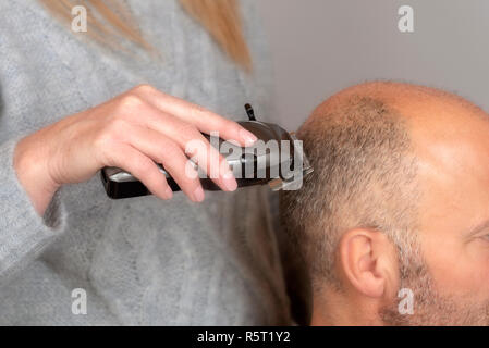 Portatili elettrici tosatrici essendo utilizzato per dare un uomo calvo un equipaggio tagliare capelli stile. Foto Stock