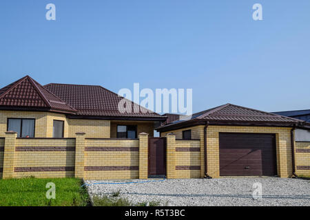 Casa di mattoni con una recinzione e cancelli. Vista di una nuova built-up recinzione e una casa fatta di mattoni e lamiera ondulata. Foto Stock