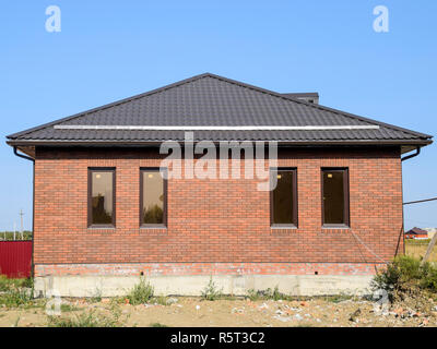 La casa con le finestre in plastica e un tetto di lamiera grecata. Tetto marrone e marrone in mattoni Foto Stock