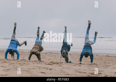 Amici facendo le verticali su una spiaggia invernale Foto Stock