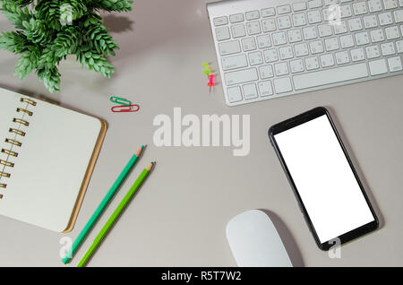 Scrivania da ufficio con computer, smart phone,notepaper e mouse con pianta in un vaso da fiori sulla parte superiore dello spazio di lavoro View. Foto Stock