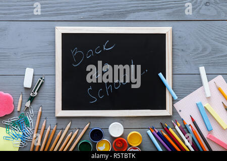 Materiali di consumo per bambini in grigio sulla scrivania in legno, torna a scuola sfondo scritta sulla lavagna per la moderna educazione primaria, anno nuovo start, matite colorate, mul Foto Stock