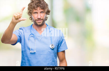 Bello ispanica medico chirurgo uomo sullo sfondo isolato sorridente e fiducioso gesticolando con la mano facendo segno di dimensione con le dita mentre cercano e Foto Stock