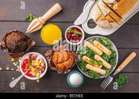 Ristorante e bar Colazione La colazione è servita con muffin, salsicce alla griglia, succo di frutta, pane fresco e parfait al buio su un tavolo di legno, vista dall'alto. Foto Stock