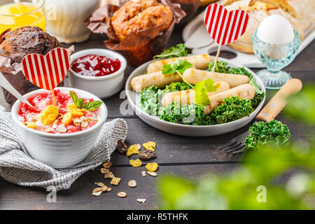 Il giorno di San Valentino del concetto. Ristorante e bar Colazione La colazione è servita con muffin, salsicce alla griglia, succo di frutta, pane fresco e parfait al buio su un tavolo di legno, lo spazio per il testo. Foto Stock