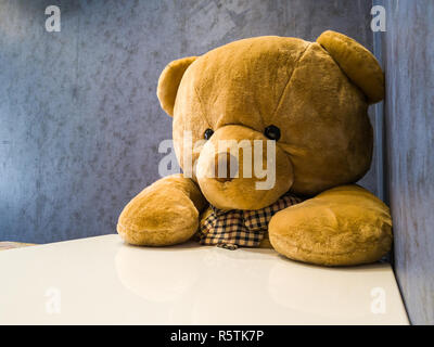 Simpatico orsacchiotto sedere sulla sedia davanti al tavolo da pranzo. Lo fanno sembrare in attesa di piatto preferito. Foto Stock