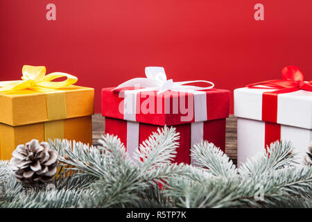 Regali di natale presenta su sfondo rosso. Neve abete bianco e rosso e oro scatole regalo con nastro archi e natalizio decorazioni. Horizo Foto Stock