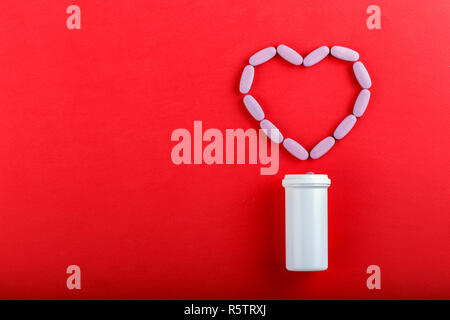 Pillole di rosa stabiliti a forma di cuore su uno sfondo di colore rosso. spazio per il testo Foto Stock