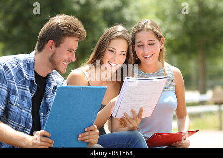 Tre felici gli studenti che studiano insieme confrontando le note in un parco del campus Foto Stock