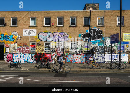 Ciclista passando edificio coperto di graffiti in Shoreditch, Londra England Regno Unito Regno Unito Foto Stock