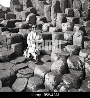 Degli anni Cinquanta, storico, una signora seduta su di un antico basalto vulcanico colonne al Giant's Causeway in Co. Antrim, Irlanda del Nord. A nord del litorale atlantico, la Causeway è una meraviglia geologica, un'area di 40.000 basalto ad incastro colonne di pietra, il risultato di una antica origine vulcanica eruzione fissurale. Foto Stock