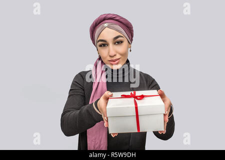 Bella giovane donna araba tenere presente nelle mani. Lei si guarda sulla fotocamera. Modello indossa hijab. Isolato su sfondo grigio Foto Stock