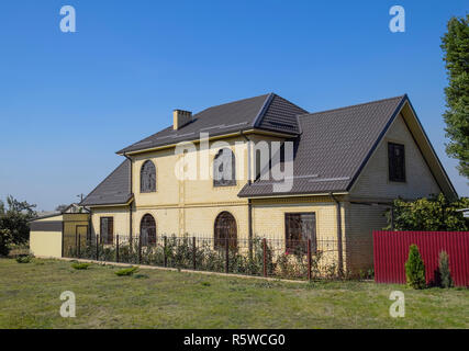 Casa del mattone giallo e marrone e tetto ondulato in metallo. Tralicci su windows. Foto Stock