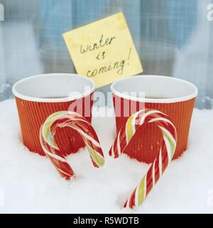 L'inverno è venuta, sfondo innevato, due natale candi canne in forma di cuore, 2 tazza di caffè. Foto Stock