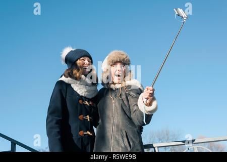 Due giovani ragazze adolescenti avendo divertimento all'aperto, sorridenti fidanzate in abbigliamento invernale tenuto selfie, persone positive e concetto di amicizia Foto Stock