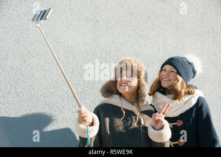 Due giovani ragazze adolescenti avendo divertimento all'aperto, sorridenti fidanzate in abbigliamento invernale tenuto selfie, persone positive e concetto di amicizia Foto Stock