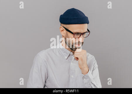 Tiro al coperto di concentrato di uomo detiene il mento e focalizzata verso il basso, essendo in profondo in pensieri, pensa idea innovativa per la sua ricerca, ha clever expr Foto Stock