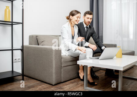 Elegante impresario e donna seduta insieme sul lettino durante il lavoro con il computer portatile a casa o in ufficio confortevole Foto Stock