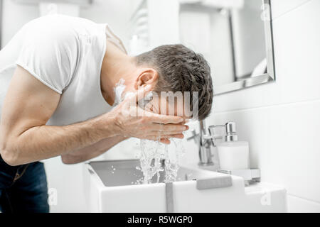 L'uomo lavare il viso con acqua fresca e la schiuma nel lavandino al bagno bianco Foto Stock