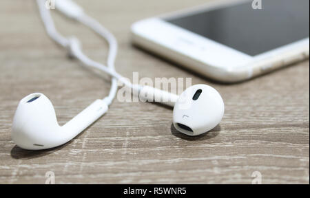 Gli auricolari bianco su una superficie di legno e lo smartphone in background. Auricolari piccoli close up Foto Stock