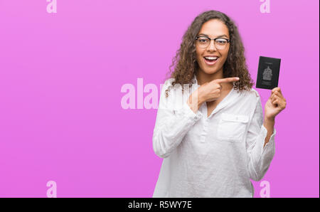 Giovane donna ispanica holding passaporto del Canada molto felice puntando con mani e dita Foto Stock