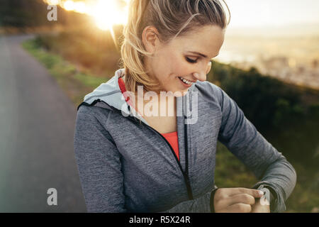 Sorridente donna fitness l'impostazione di un temporizzatore nel suo orologio da polso in piedi all'esterno. Runner tempo di controllo nel suo orologio durante la sua corsa mattutina. Foto Stock