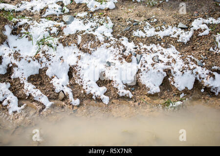 Il bianco della neve sui rocciosi e fangosi superficie in inverno Foto Stock